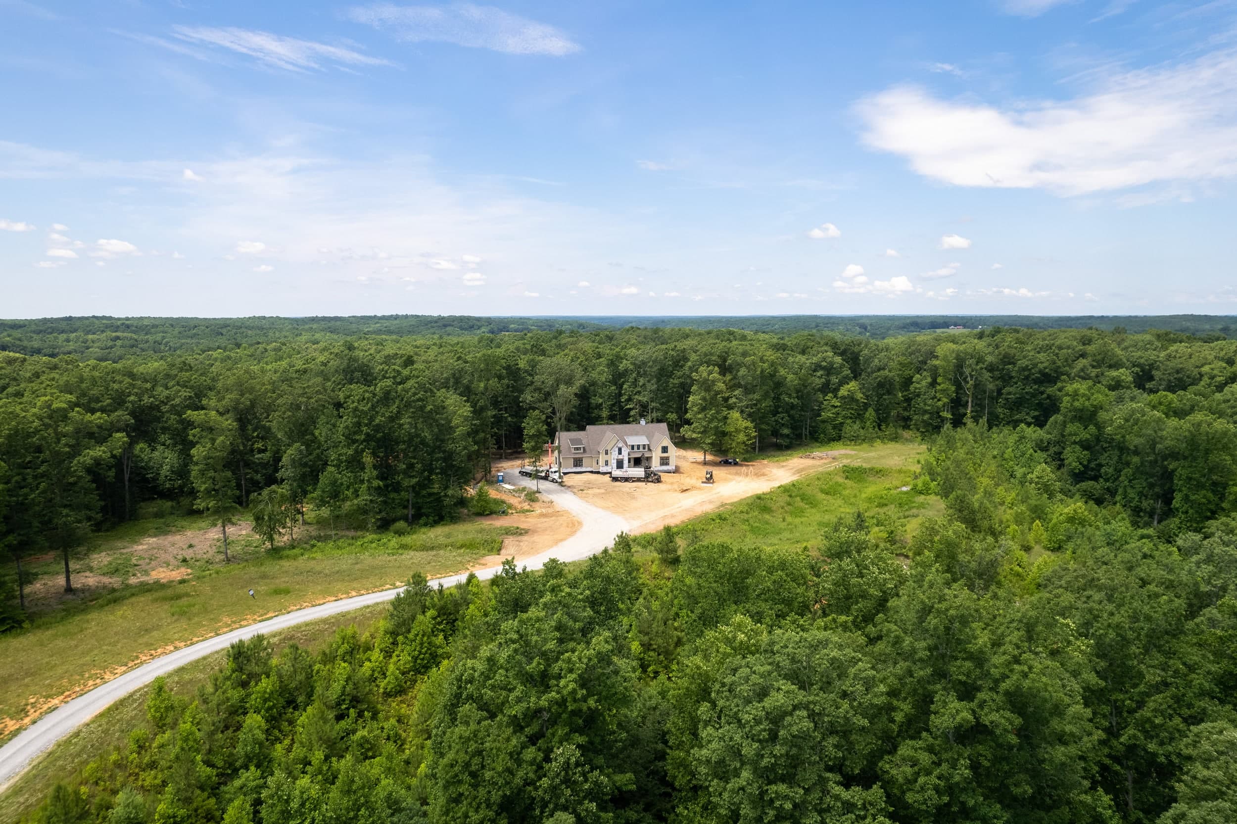 Aerial view of a home under construction on a cleared, hilly Tennessee lot with forested surroundings