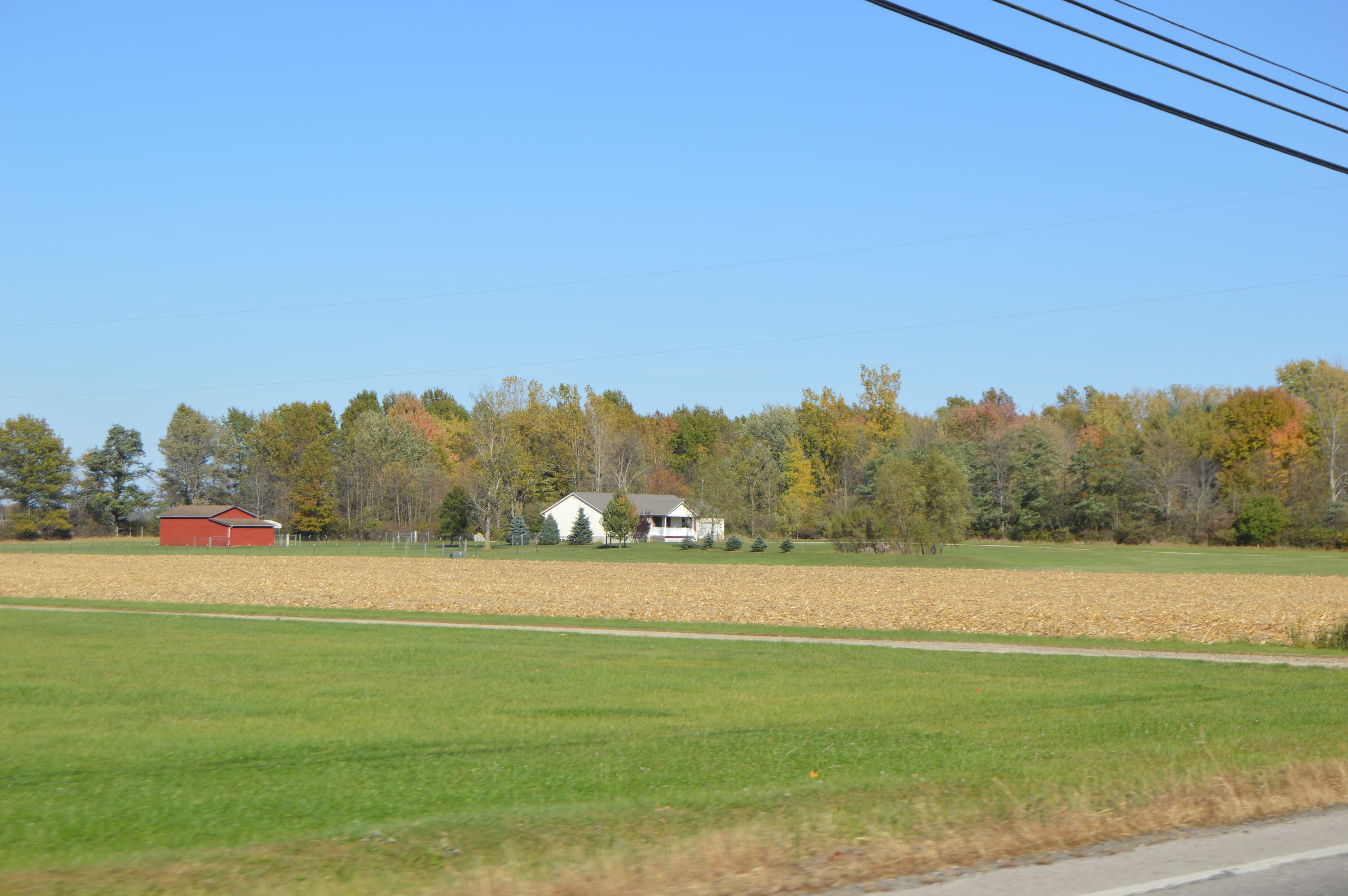 Power lines running across rural farmland with a red barn and farmhouse